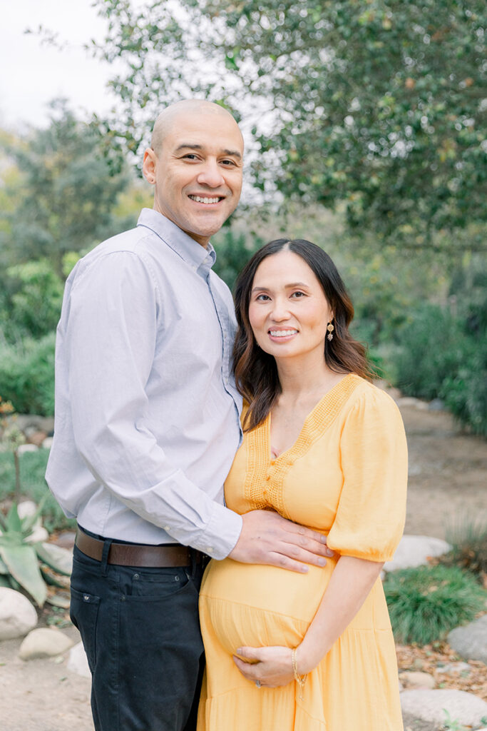 Expecting couple smiling during their maternity session at the Secret Garden in Huntington Central Park, Huntington Beach