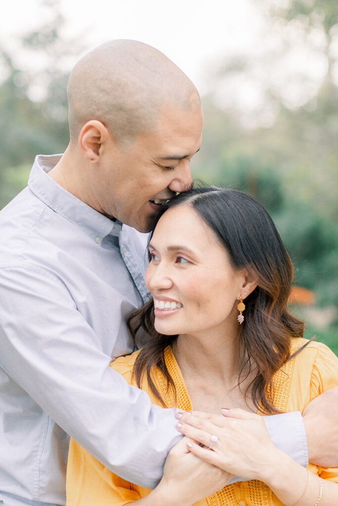 Joyful maternity moment with husband embracing his pregnant wife from behind at the Secret Garden in Huntington Central Park, Huntington Beach