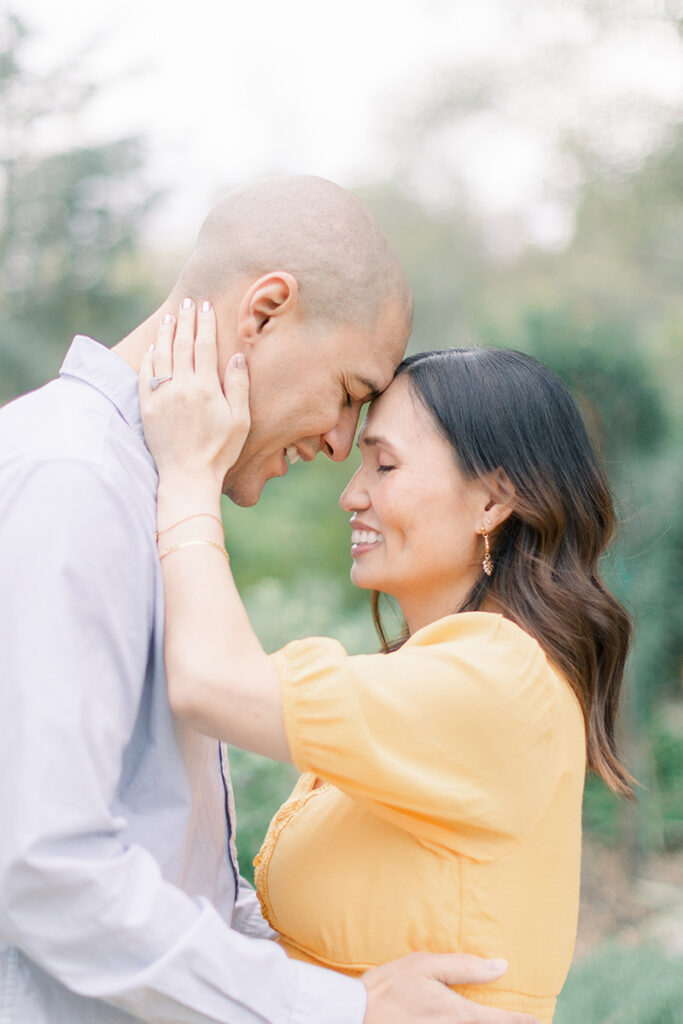 Close-up of expecting couple smiling with foreheads touching during their maternity session at Huntington Central Park's Secret Garden in Huntington Beach