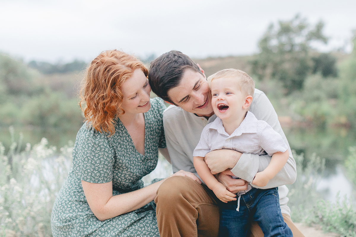 Mom and Dad laughing with their toddler son during a joyful family photo session at Eagle Scout Lake in Kit Carson Park, San Diego