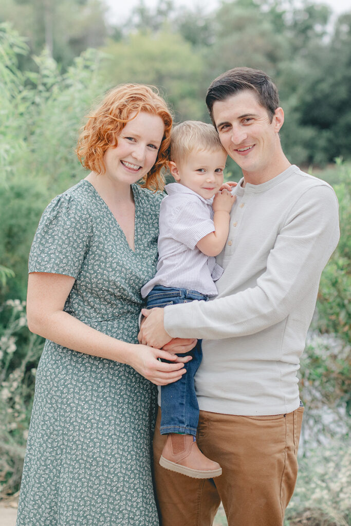 Smiling family of three during a natural light photo session at Eagle Scout Lake in Kit Carson Park, North County San Diego