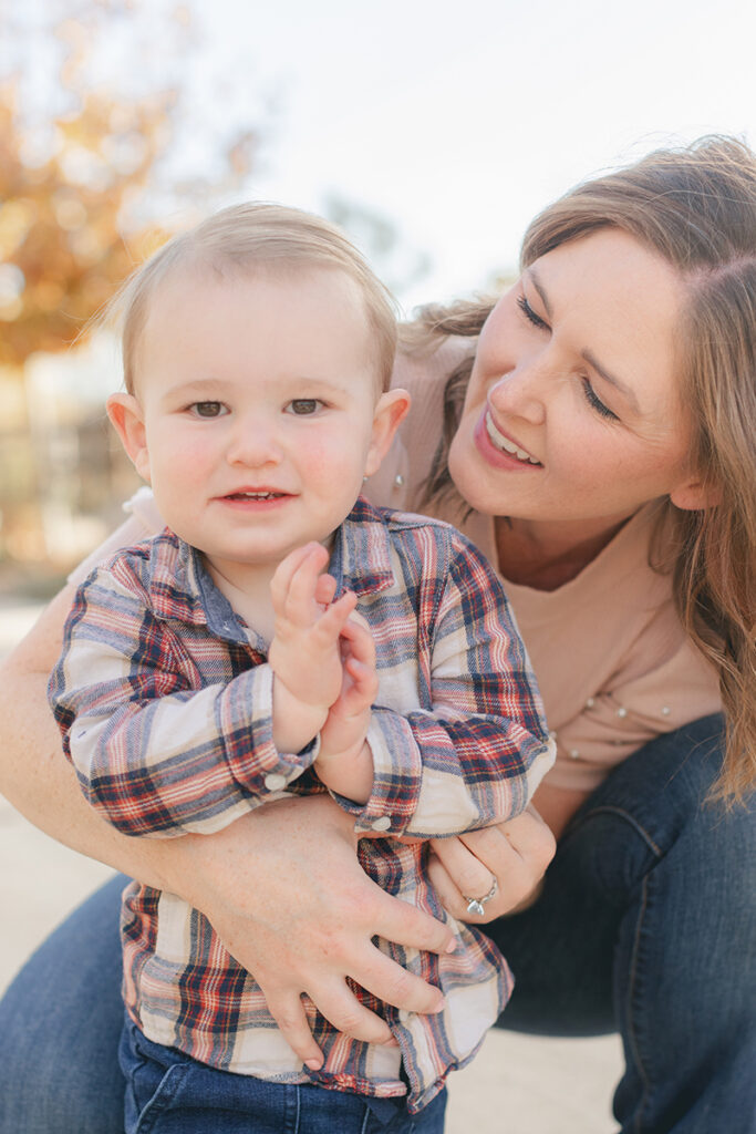 Close-up of a mother smiling at her toddler son as he claps his hands, both enjoying a joyful moment during their fall family session in Santee, California.