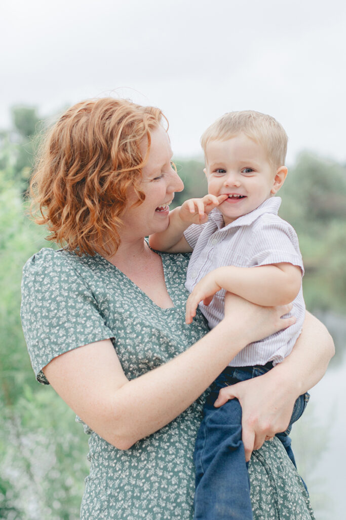Mom laughing while holding her toddler during a joyful family photo session at Kit Carson Park in North County San Diego