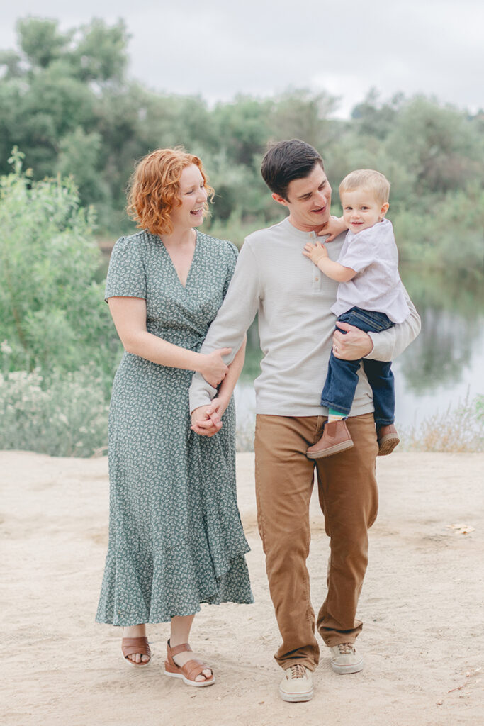 A young family walking together near Eagle Scout Lake in Kit Carson Park, North County San Diego, during a natural light family photo session