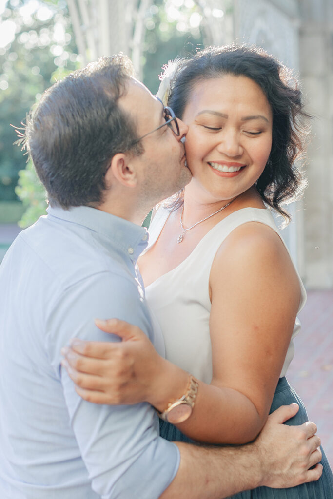 Guy kissing girl on the cheek as she smiles during a romantic engagement session at Greystone Mansion in Beverly Hills, California.