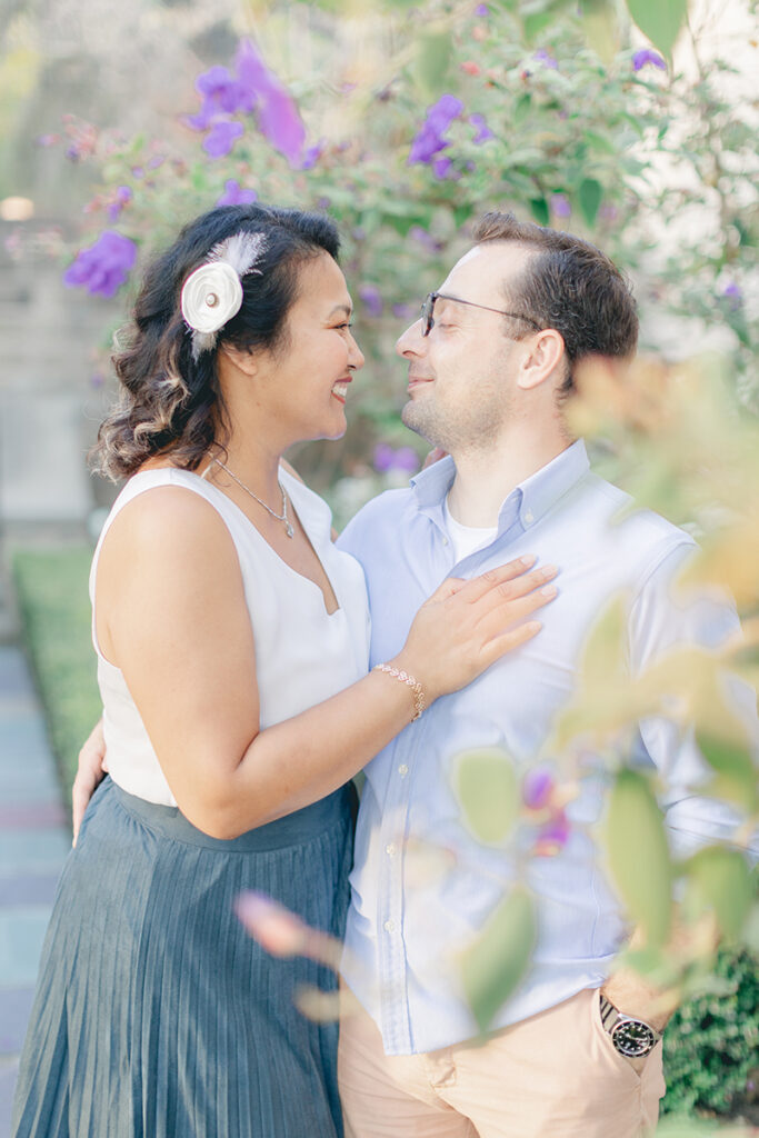 Engaged couple smiling at each other surrounded by blooming purple flowers during a romantic garden engagement session at Greystone Mansion in Beverly Hills.