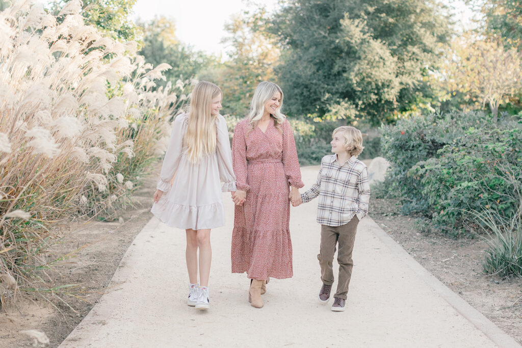 Mom walking hand in hand with her daughter and son along a natural trail at Encinitas Community Park during a family photography session in San Diego