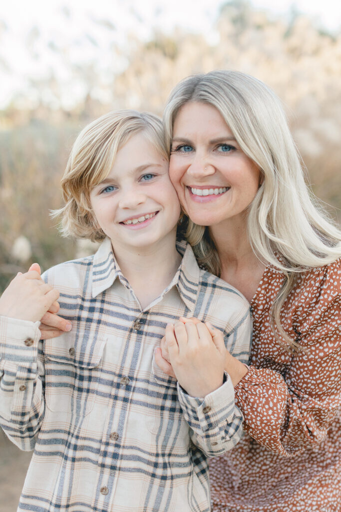 Close-up of a smiling mom and her school-age son holding hands during a San Diego family photography session at Encinitas Community Park