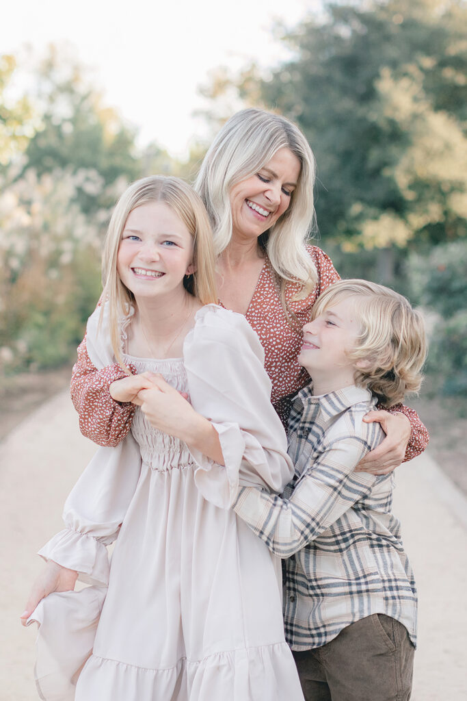 Smiling mom hugging her daughter and son during a joyful family photography session at Encinitas Community Park in San Diego