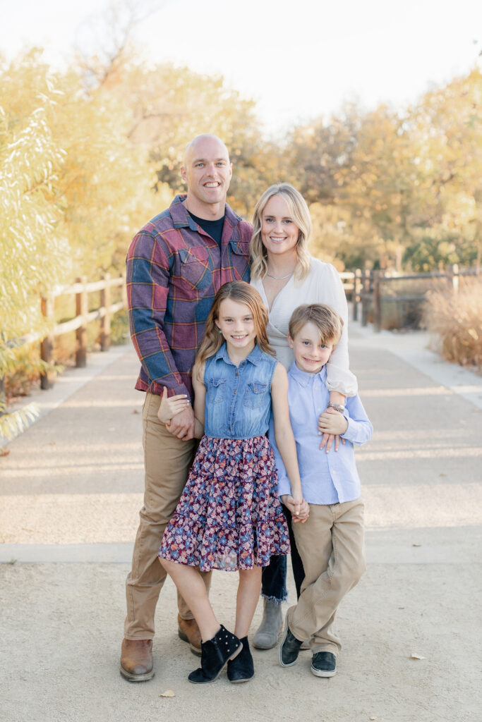 Family of four smiling during a San Diego fall mini session with beautiful golden autumn trees.