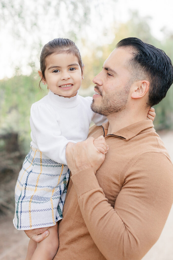 Father holding his young daughter during a family photoshoot at Montevalle Park in Chula Vista, both smiling and dressed in cozy fall outfits