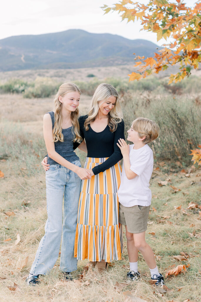 Smiling mom standing with her daughter and son during a fall family photo session in San Diego with mountains and autumn foliage in the background
