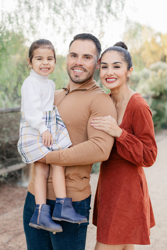 Smiling family of three posing together during a fall photoshoot at Montevalle Park in Chula Vista, with coordinated outfits and natural light
