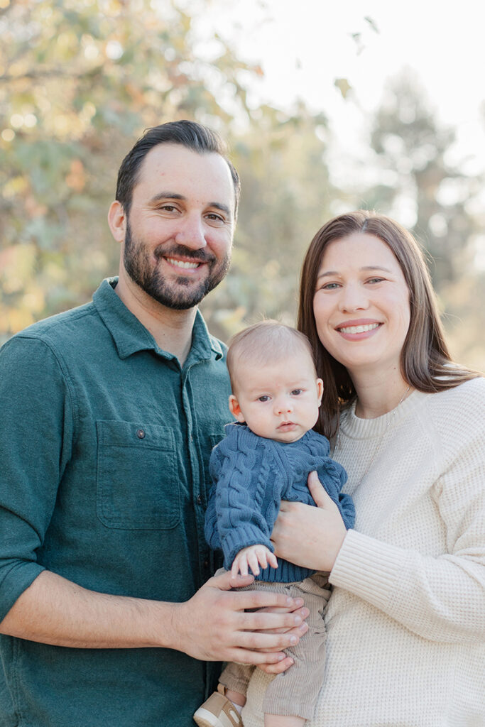 Close-up family portrait of parents smiling with their three-month-old baby during a golden hour session in La Mesa, San Diego, with soft natural light and autumn background.