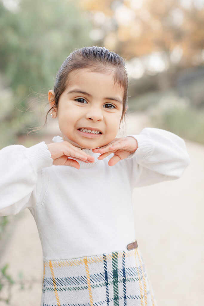 Young girl smiling sweetly with hands under her chin during a family photoshoot at Montevalle Park in Chula Vista