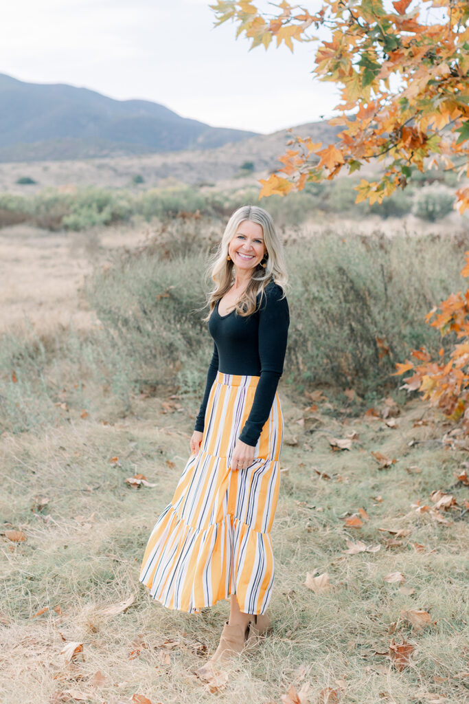 Portrait of a smiling woman standing in a field during a fall photo session in San Diego with natural light and autumn colors in the background