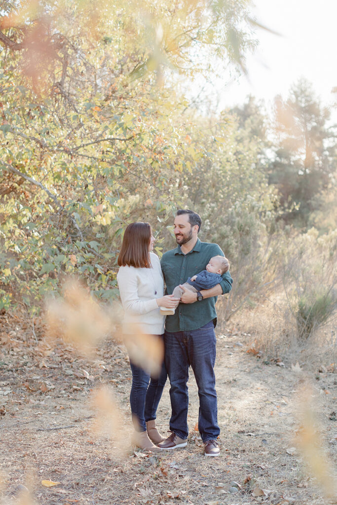 Young family with a newborn baby during a golden hour photo session at Harry Griffen Park in La Mesa, San Diego, surrounded by soft autumn foliage and natural light.