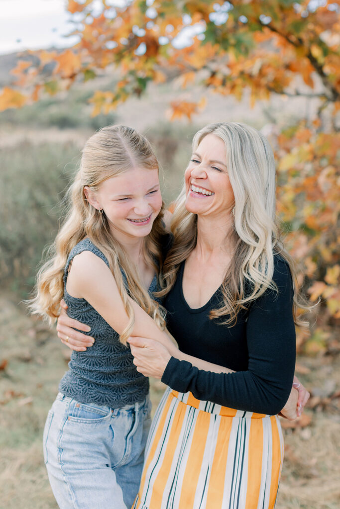 Mom and daughter laughing and hugging during a fall mini session in San Diego with autumn leaves in the background